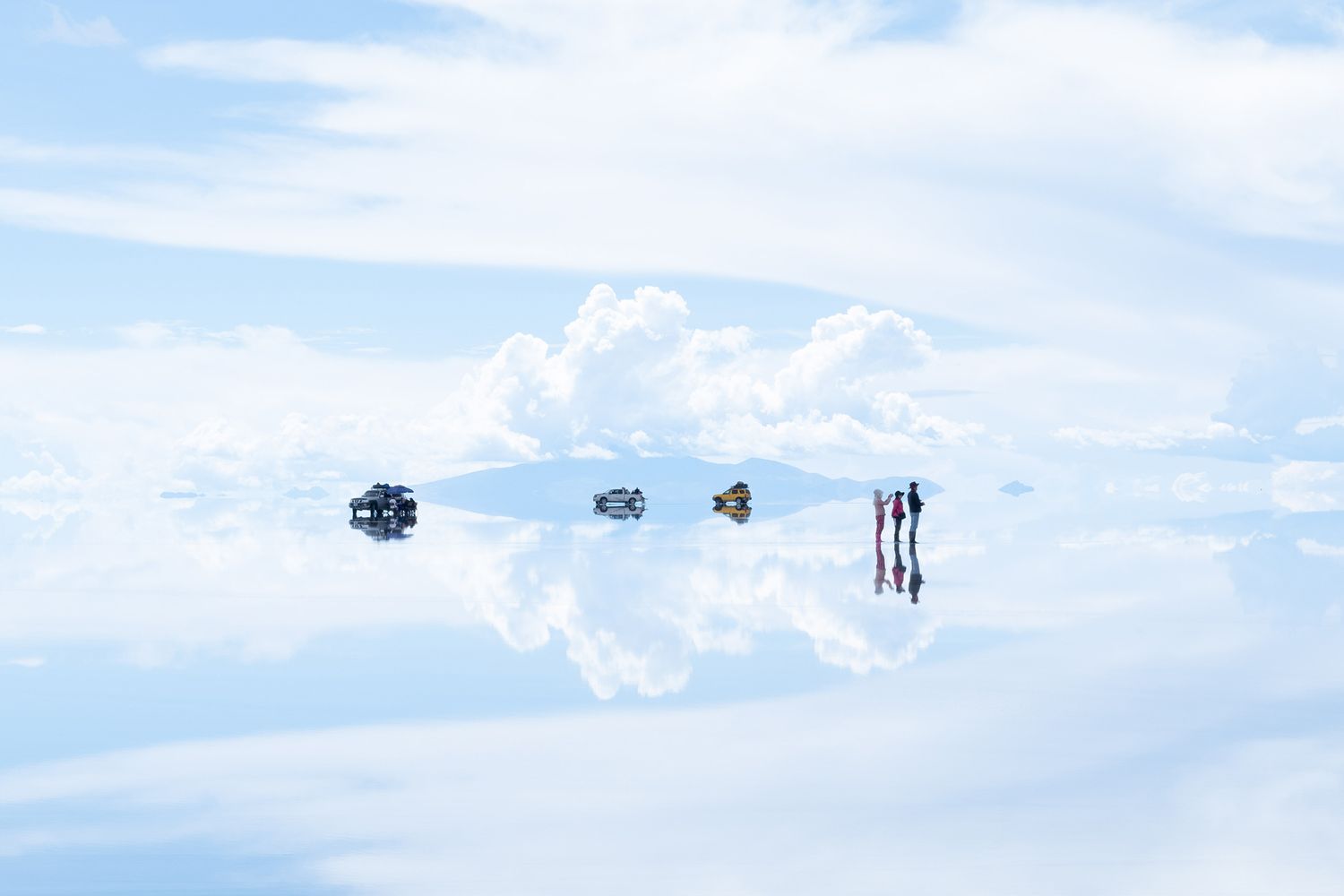 انعکاس خودروها و افراد روی دشت نمک زیر آسمان وسیع و ابری